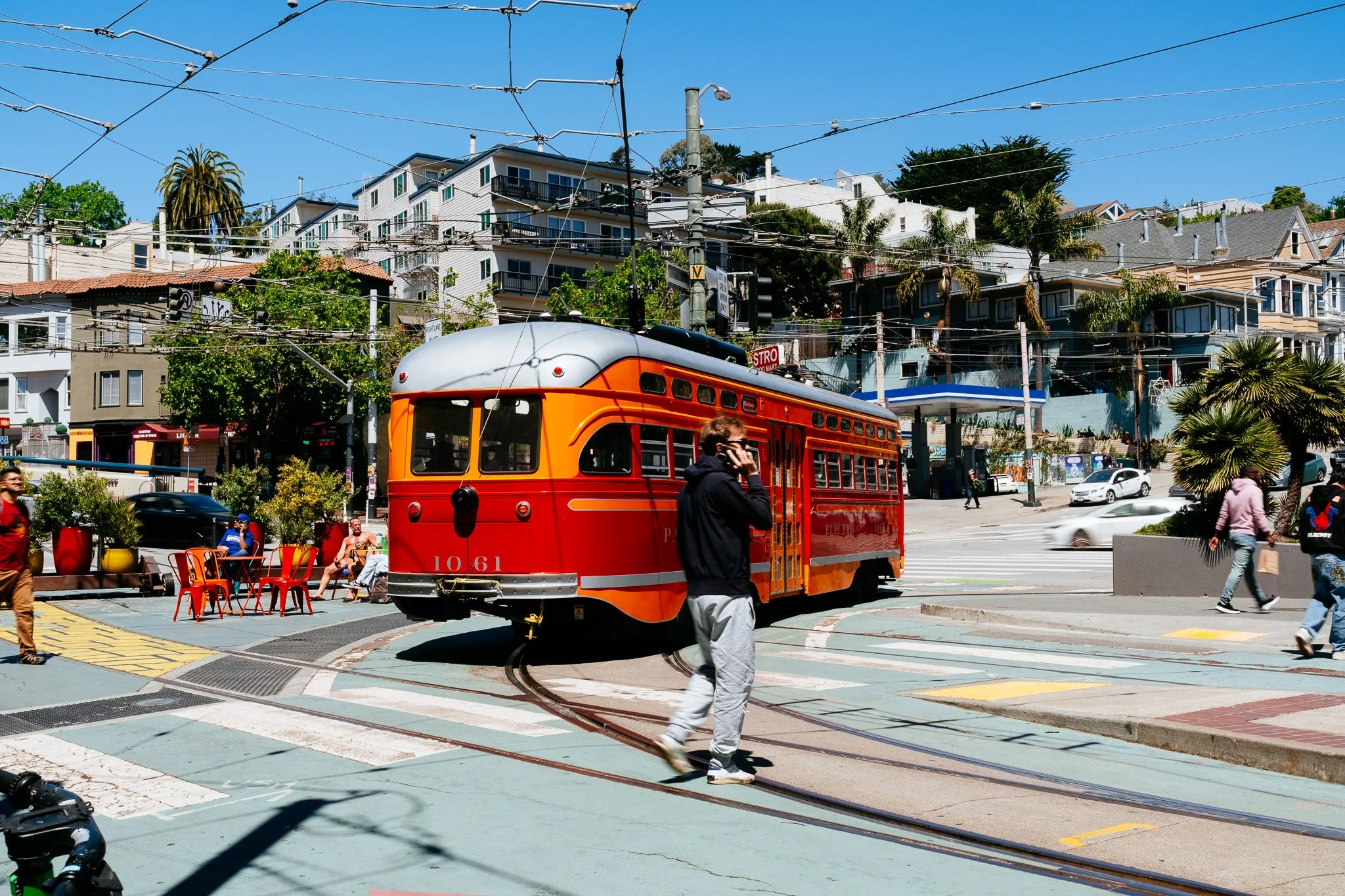 Vintage orange F-line streetcar rounding a sunny Castro intersection as a pedestrian crosses