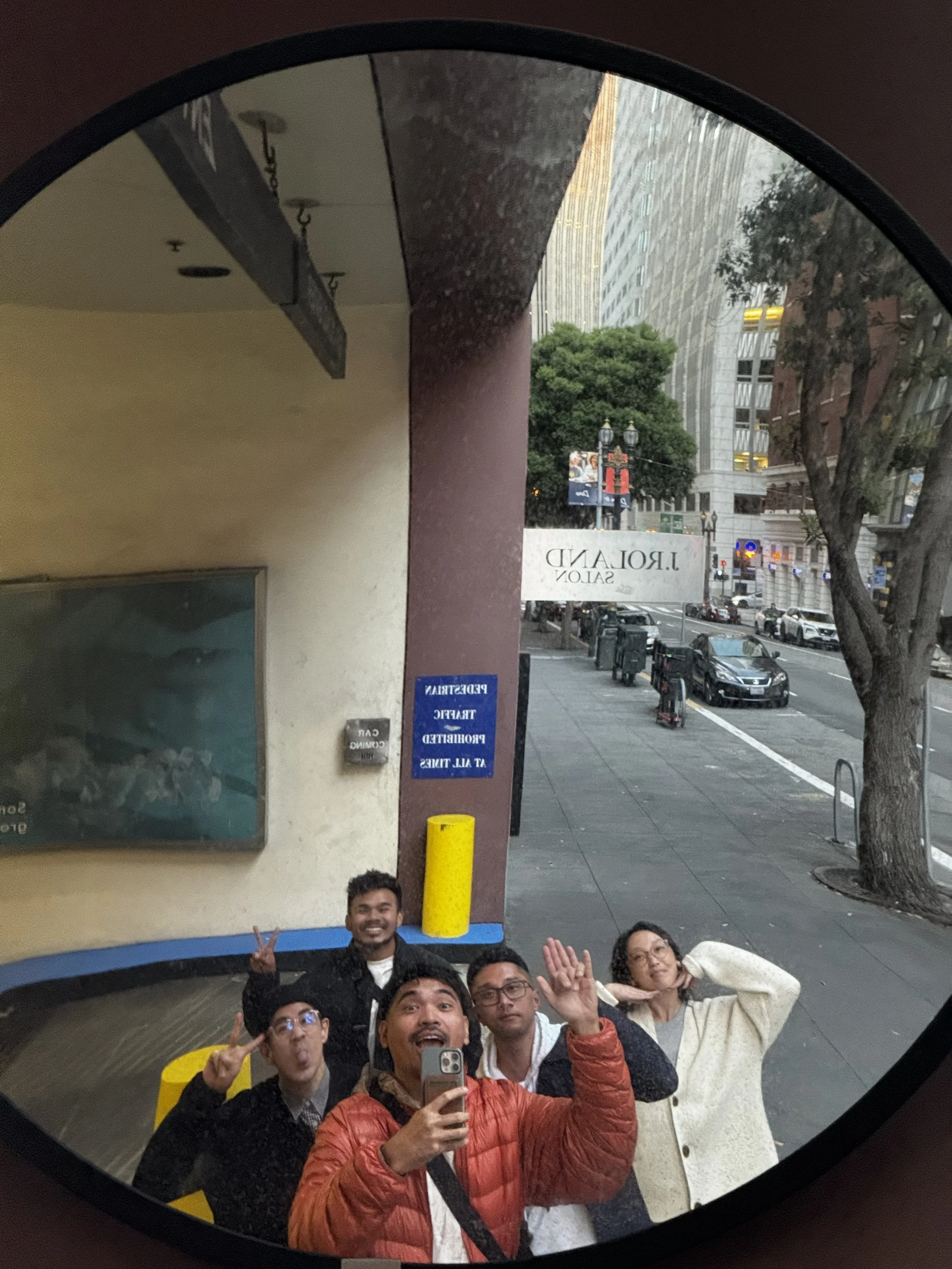 Five friends waving and making faces into a round convex mirror on a San Francisco street