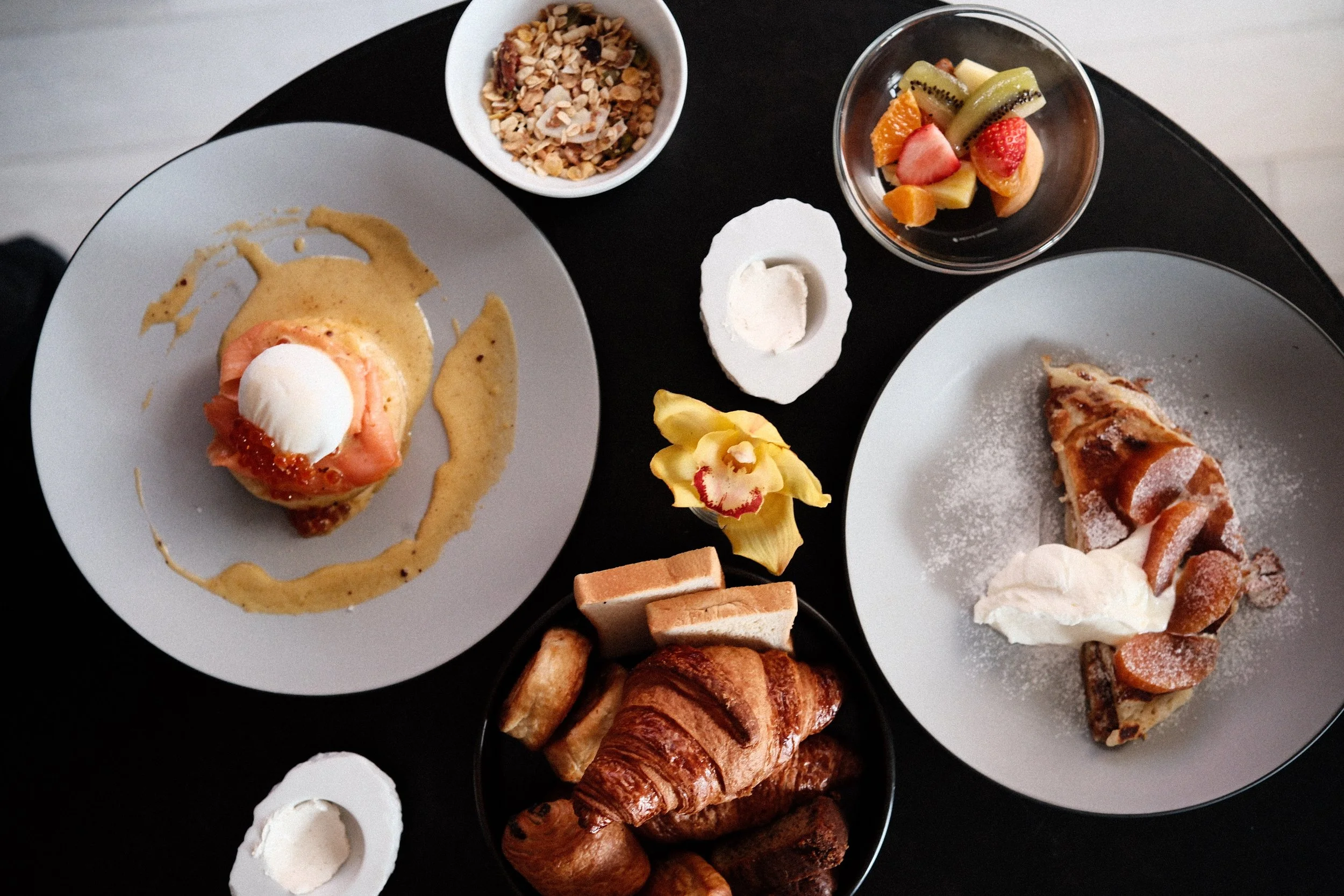 Overhead view of a hotel breakfast with croissants, granola, fruit and salmon pancakes