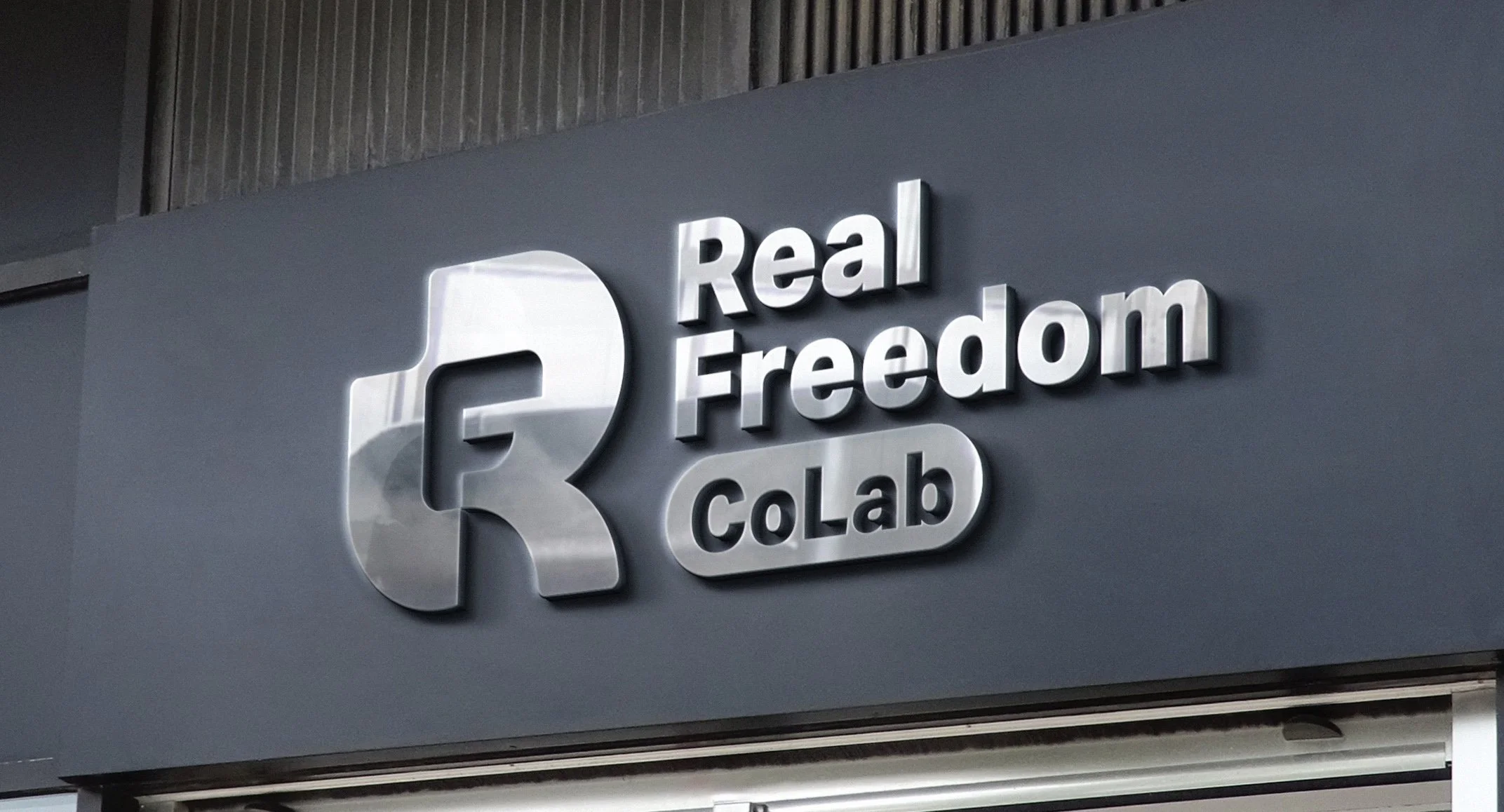 Real Freedom CoLab monogram logo rendered as brushed metal storefront signage mockup