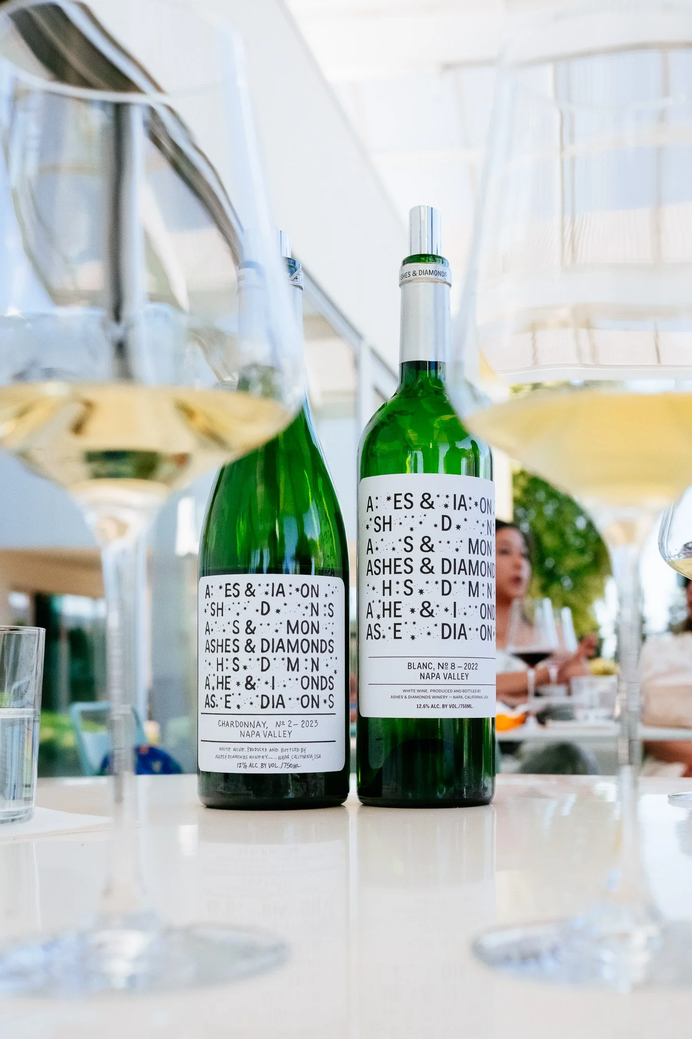 Two Ashes & Diamonds Napa Valley white wine bottles flanked by glasses of chardonnay