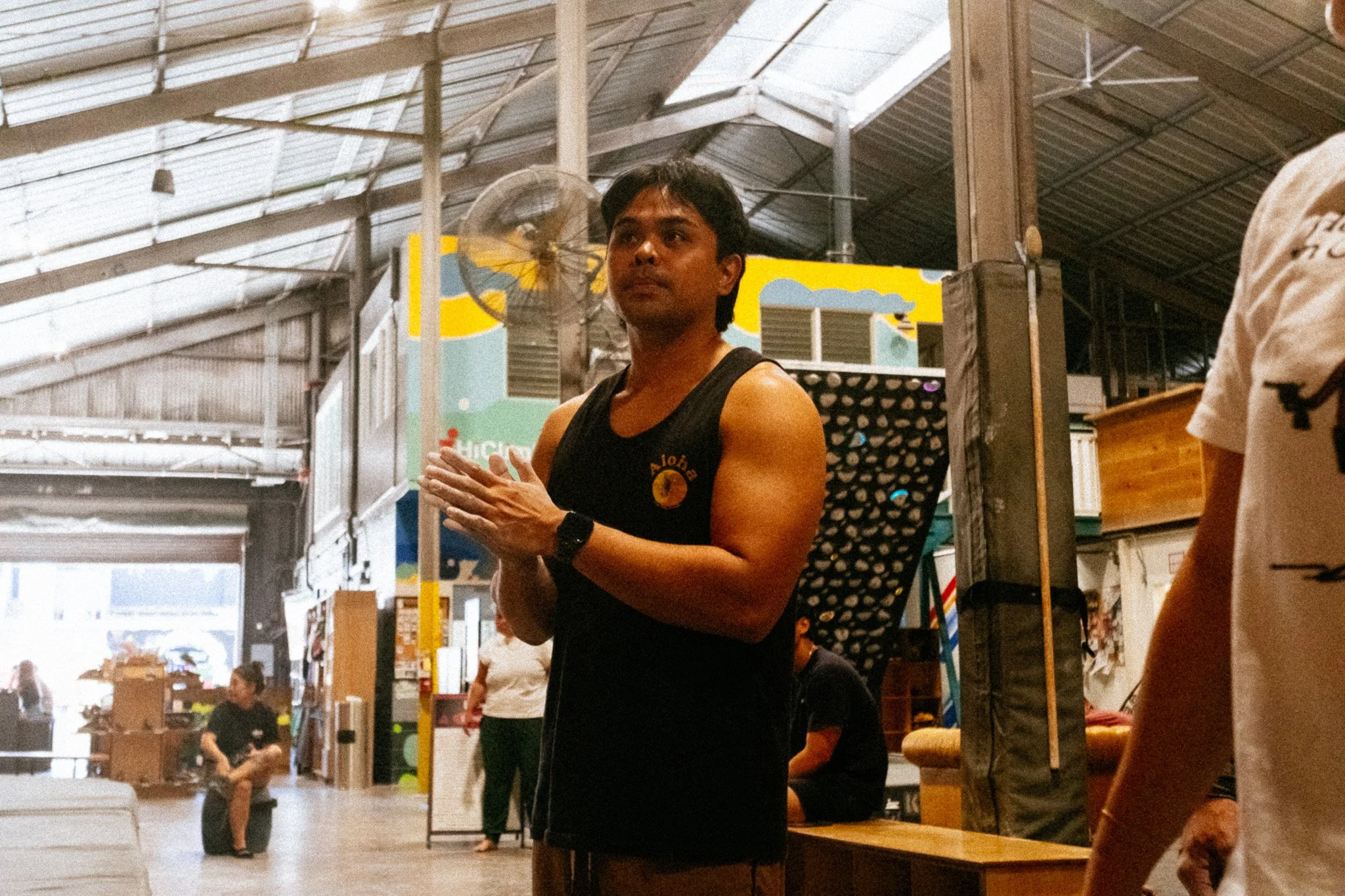 Climber in an aloha tank top clapping chalked hands inside a Honolulu climbing gym