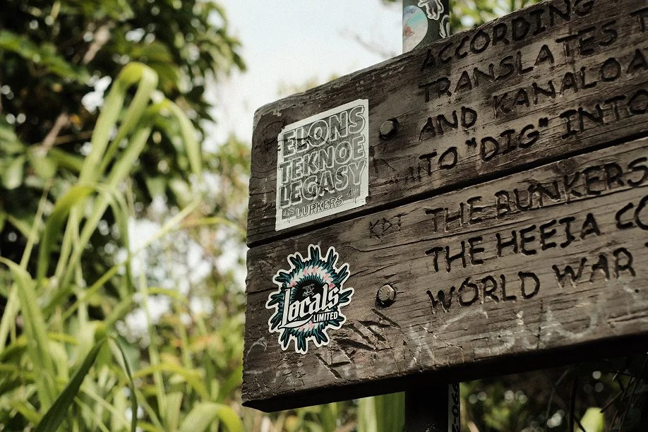 Weathered carved wooden trail sign describing the Heeia World War II bunkers, covered in stickers