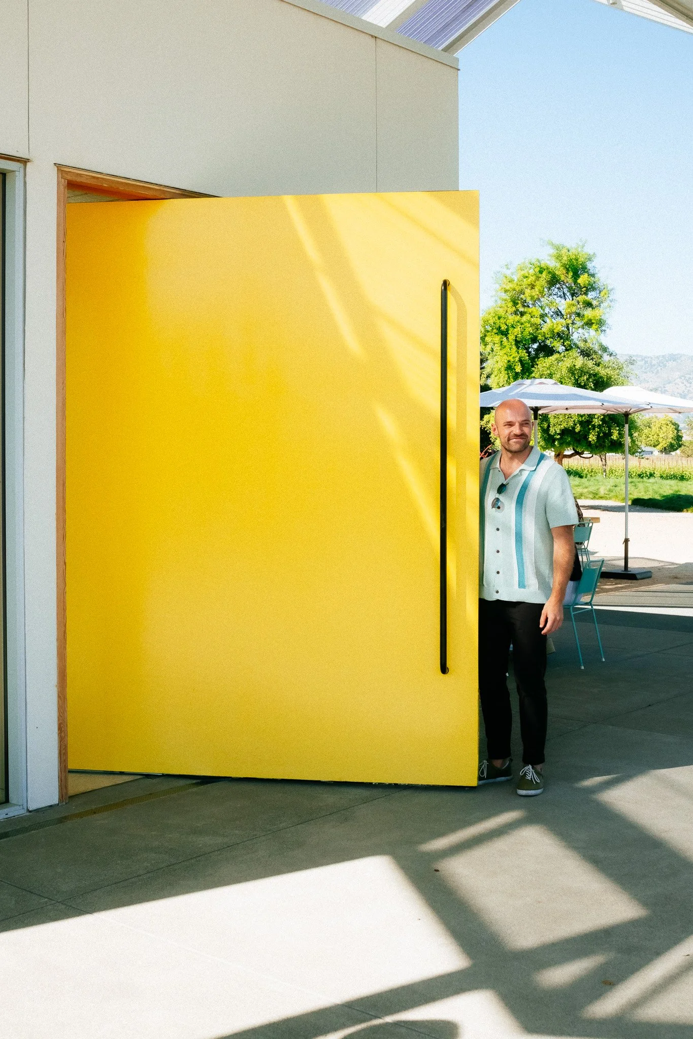 A friend peeking from behind the giant yellow pivot door at a Napa winery tasting room