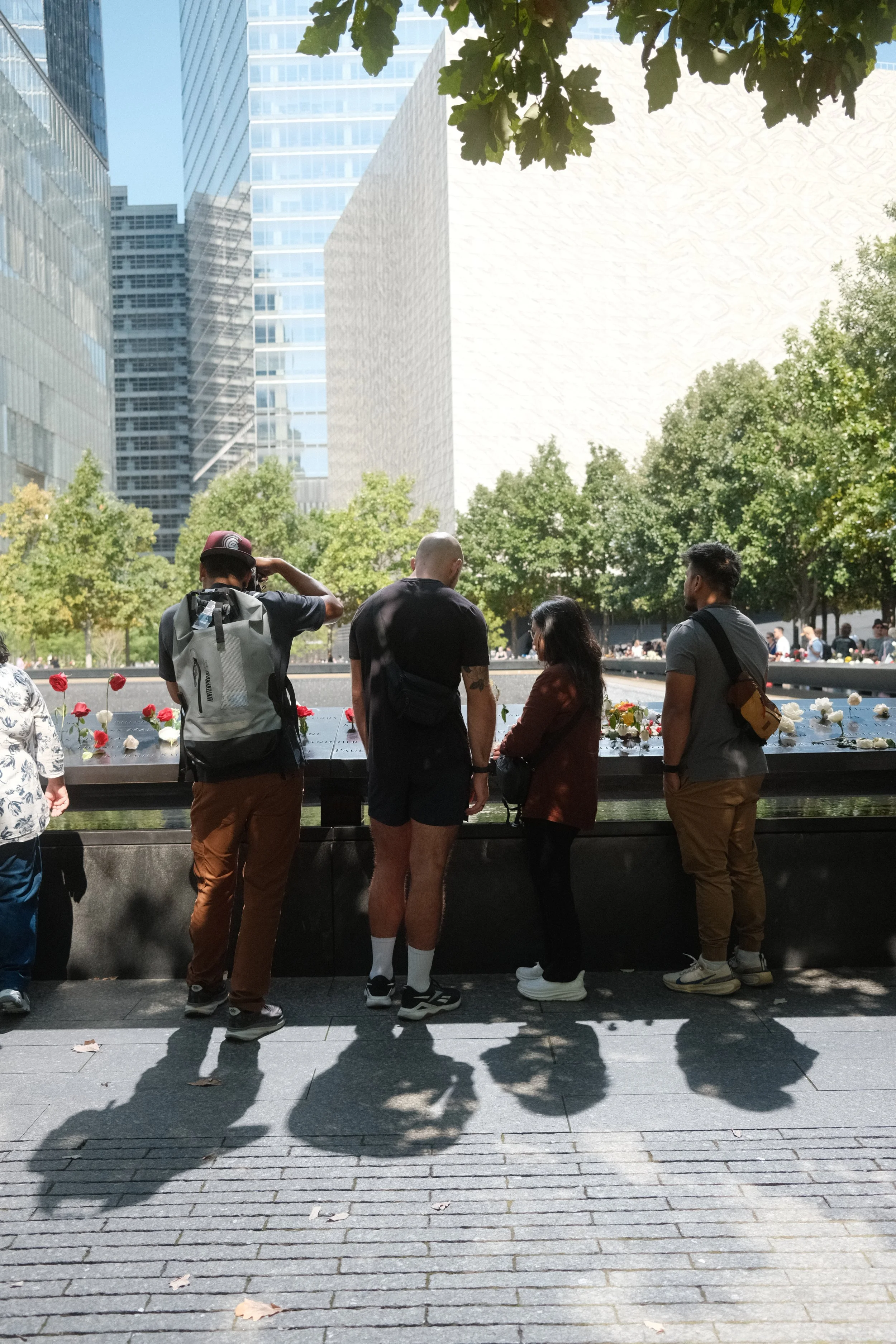 Visitors at a 9/11 Memorial pool with roses tucked into the engraved names