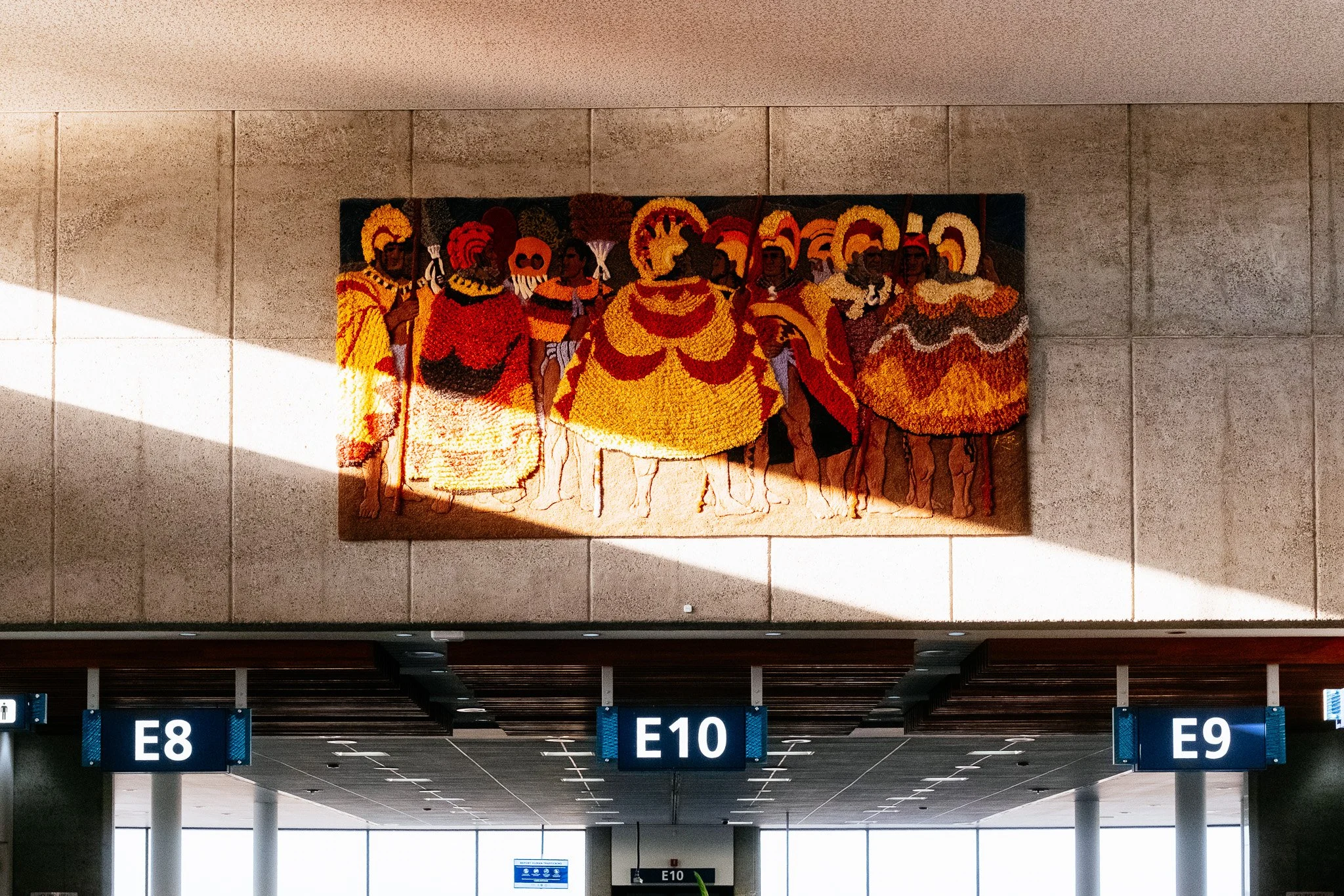 Colorful mural of Hawaiian alii in feather cloaks above gates E8 to E10 at Honolulu airport
