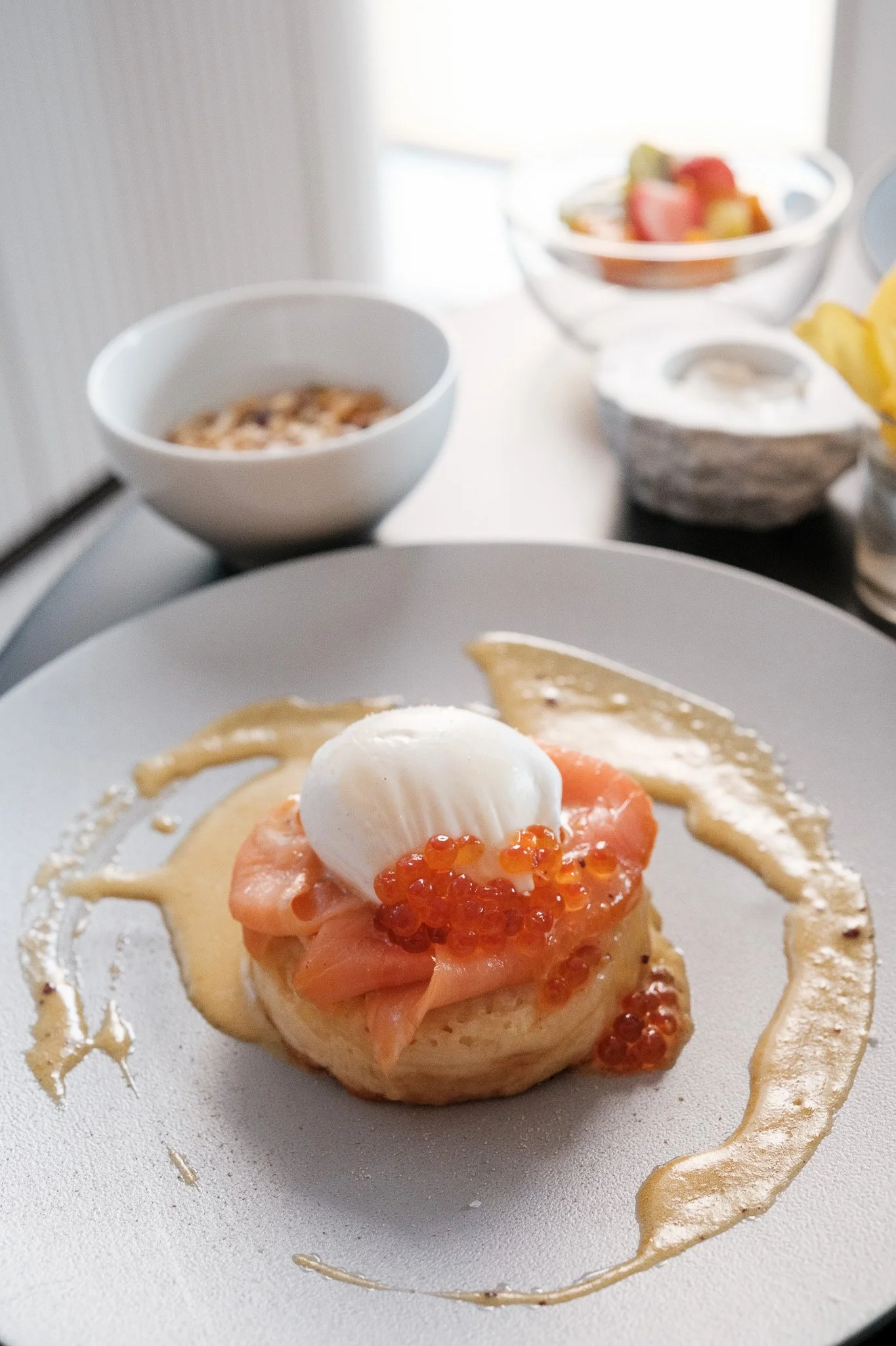 Fluffy pancake topped with smoked salmon, ikura and a poached egg on a gray plate