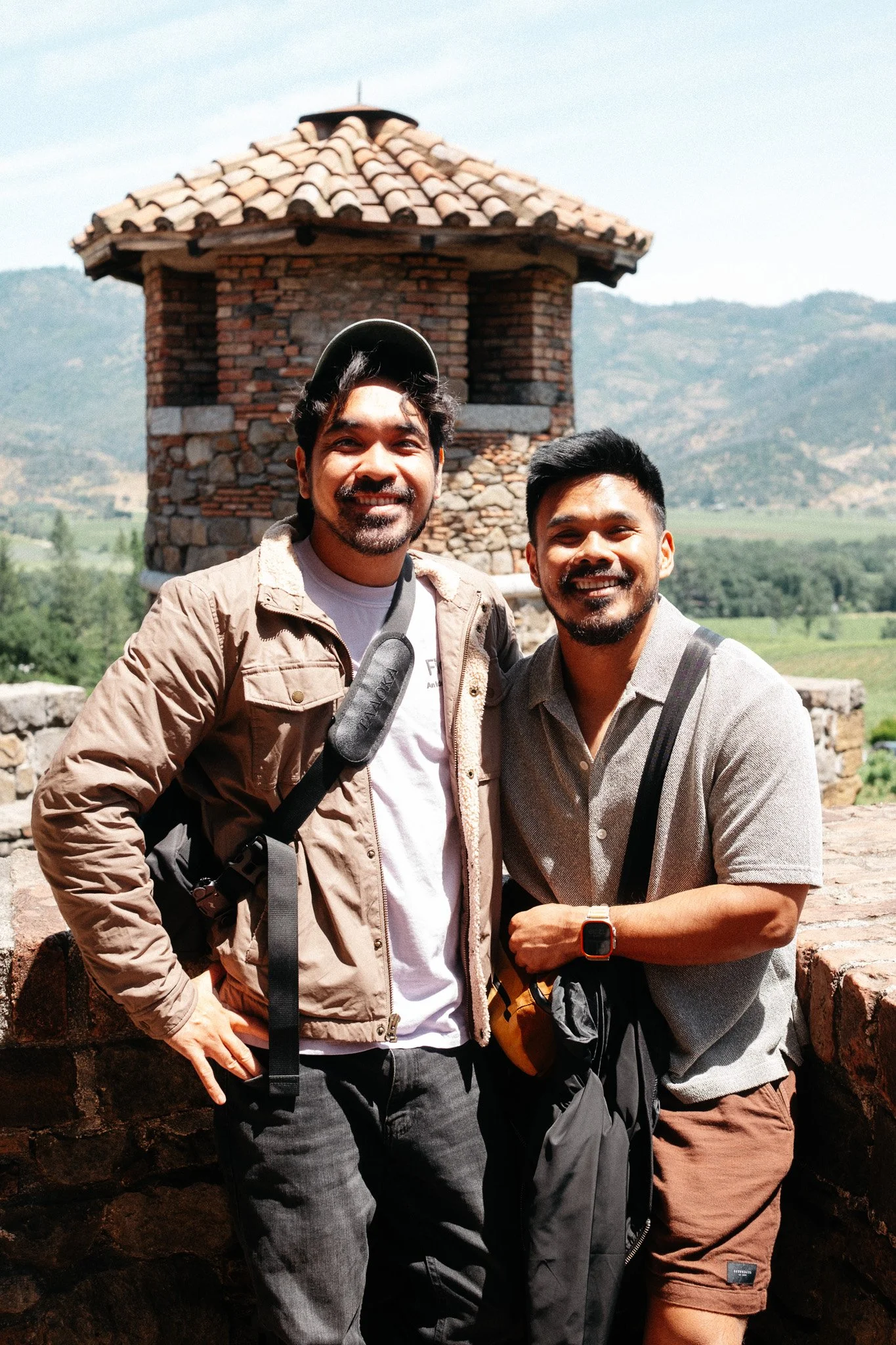 Two smiling friends posing at a stone turret overlooking Napa Valley hills