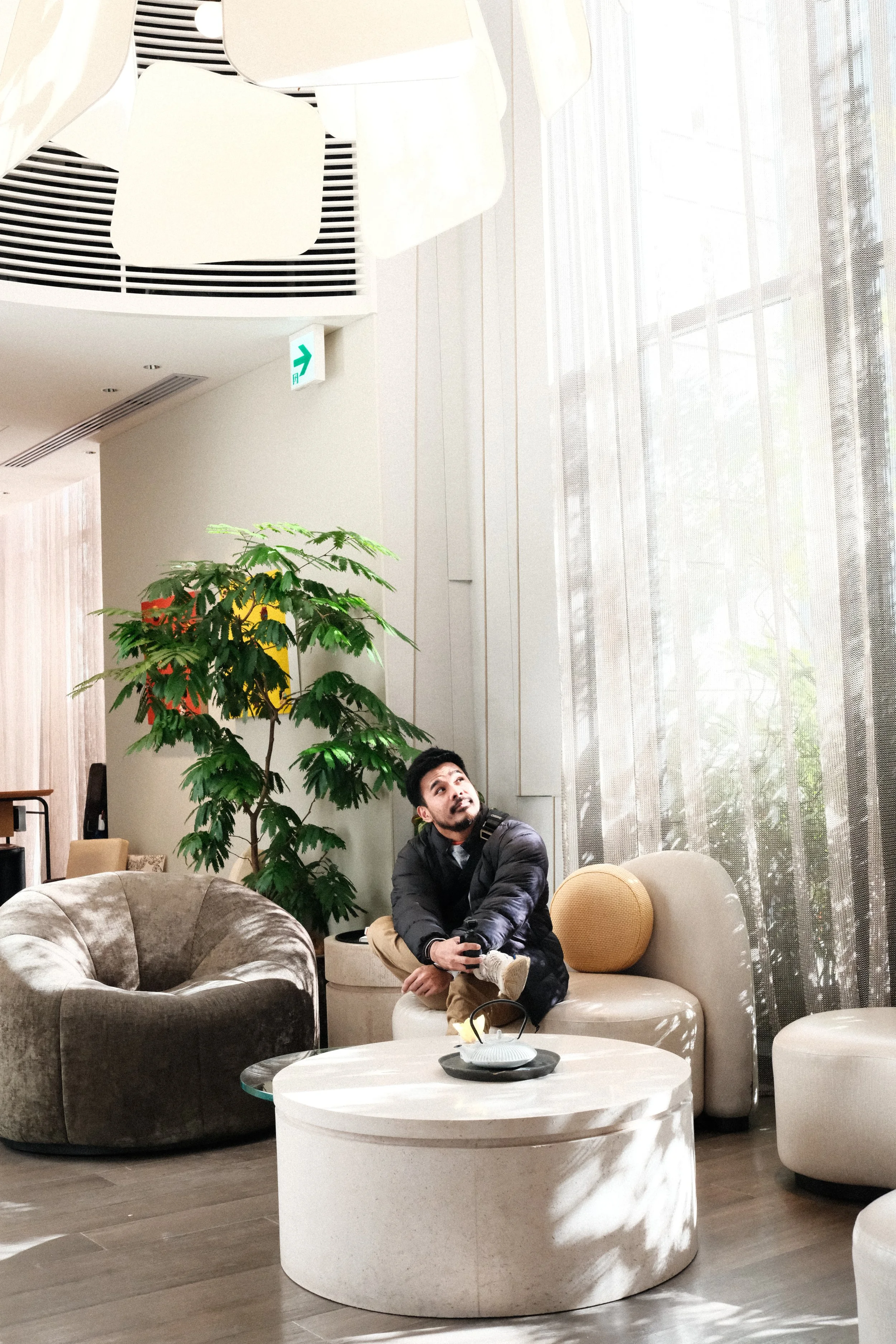 Mark sitting cross-legged on a curved sofa in a bright Tokyo hotel lounge