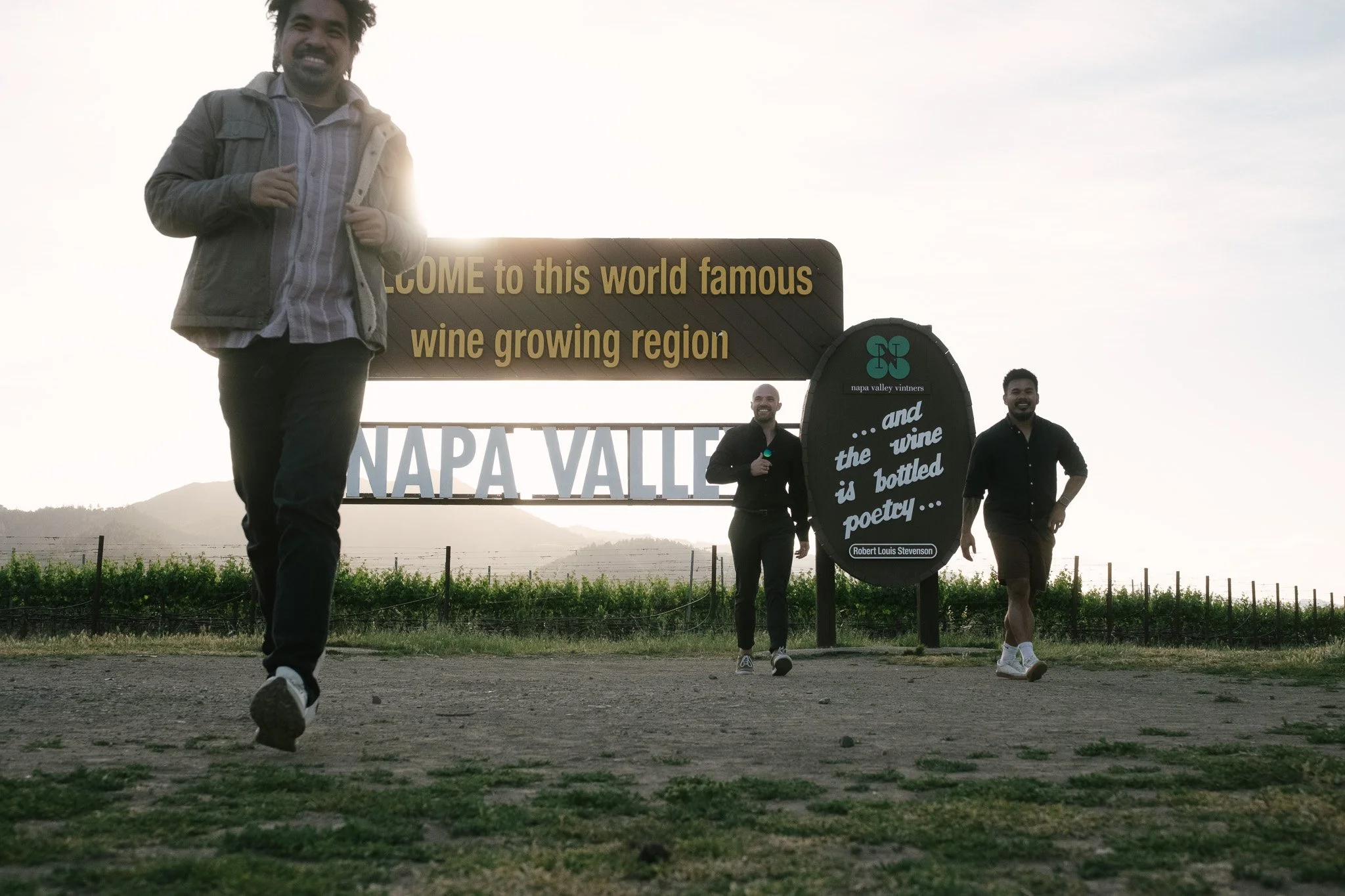 Three friends running toward the camera from the Welcome to Napa Valley sign at sunset