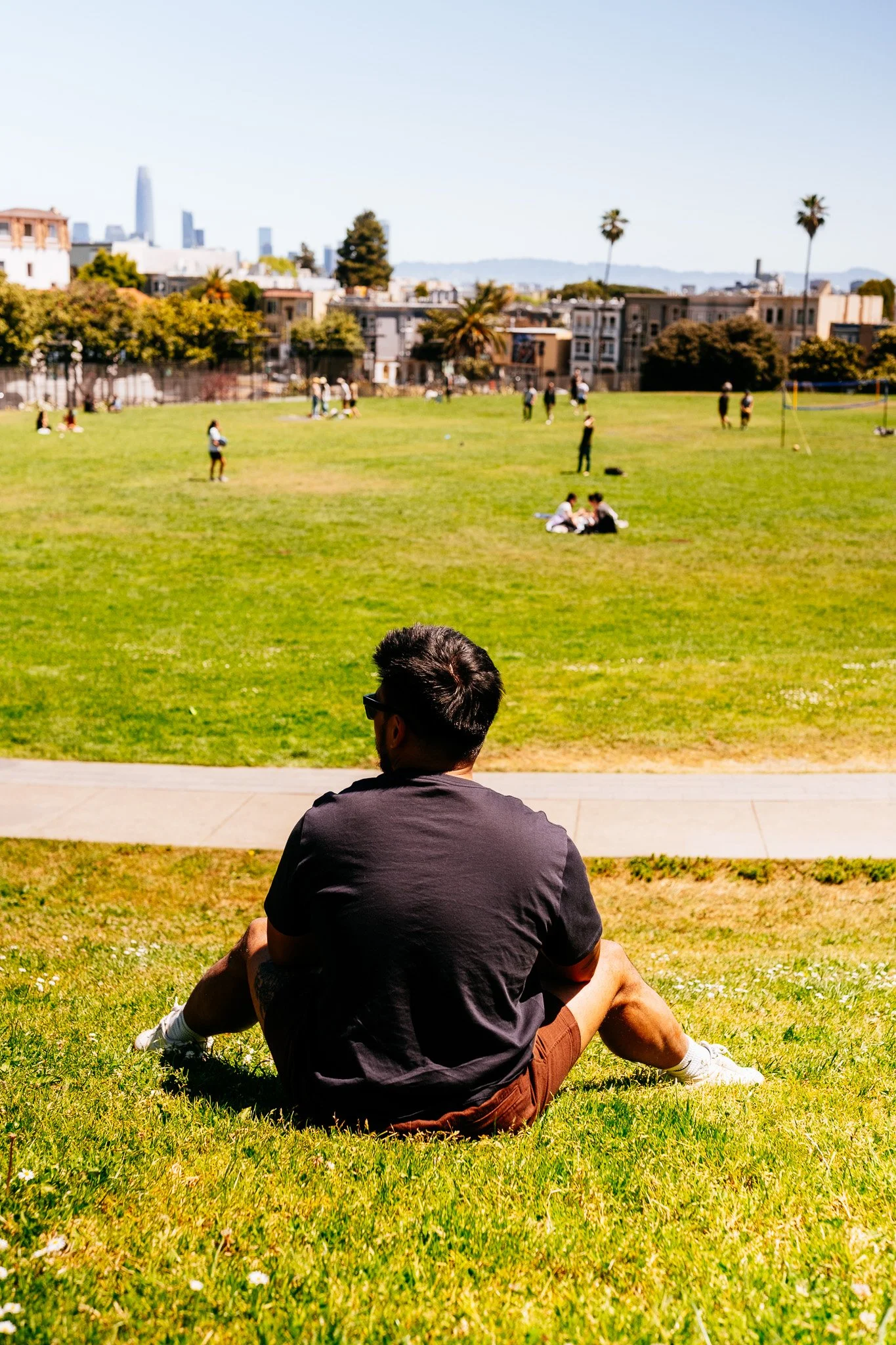 Man sitting on the grass at Dolores Park with the San Francisco skyline in the distance