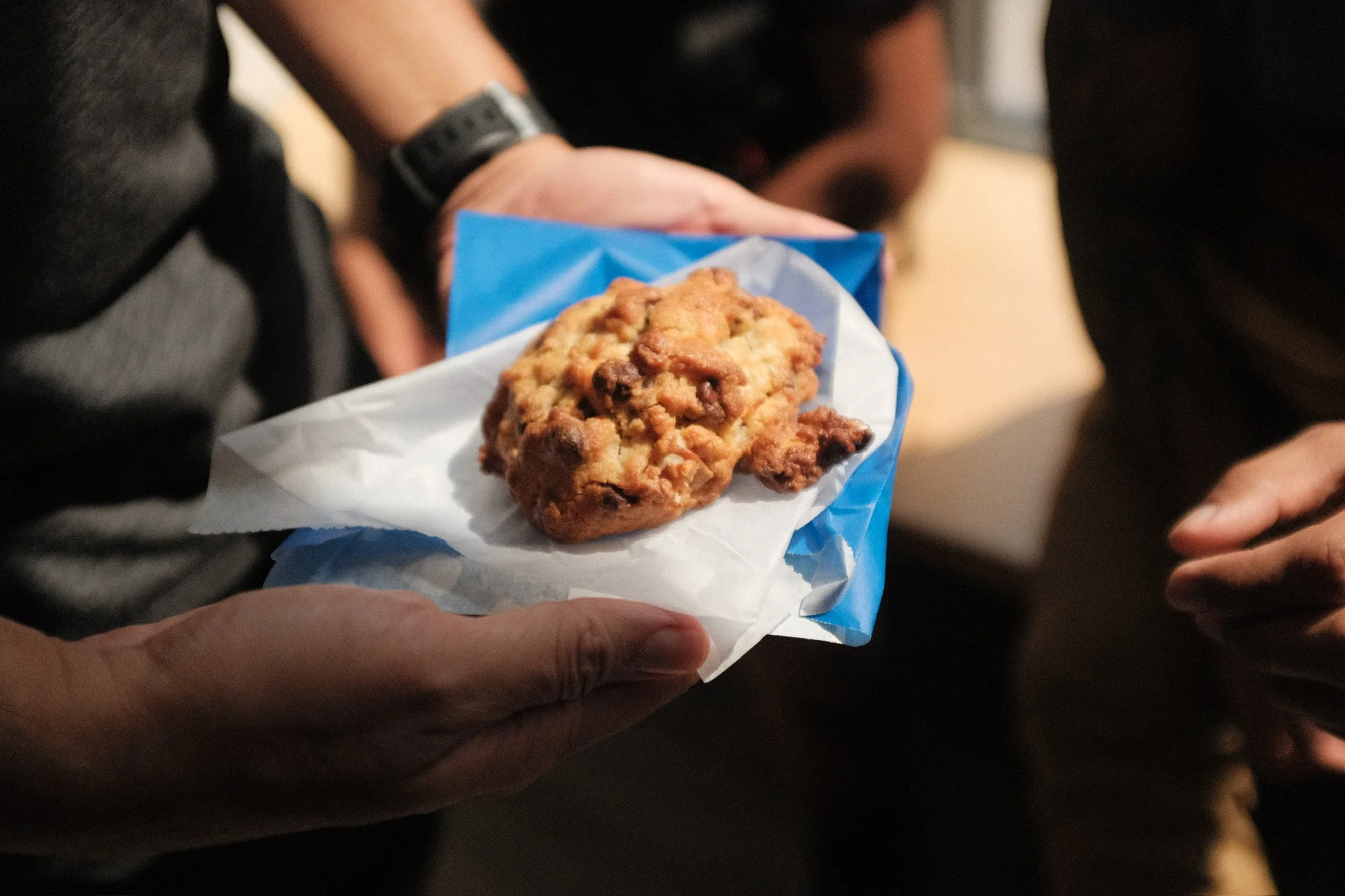 Hands holding a chunky chocolate chip cookie in bakery paper