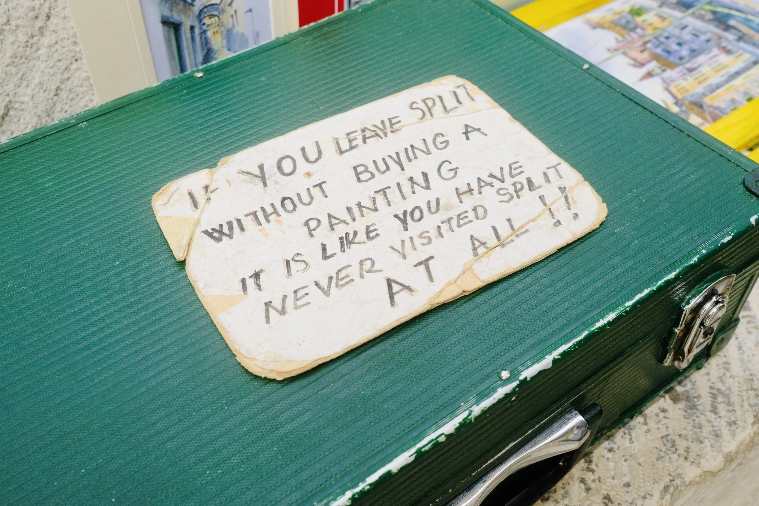 Handwritten sign in Split saying leaving without buying a painting is like never visiting