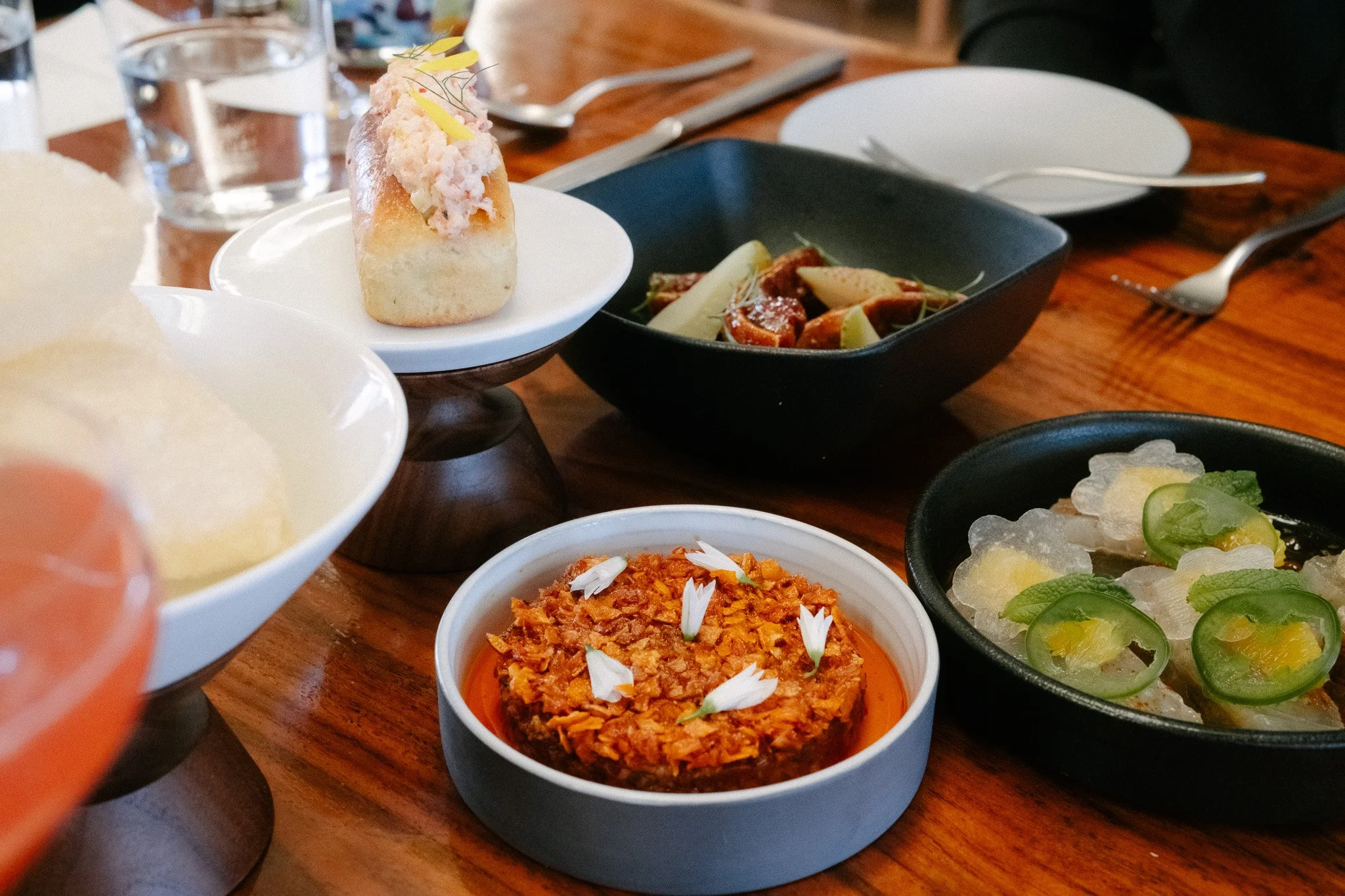 Table of small plates including a mini lobster roll, tartare and crudo at a Napa restaurant
