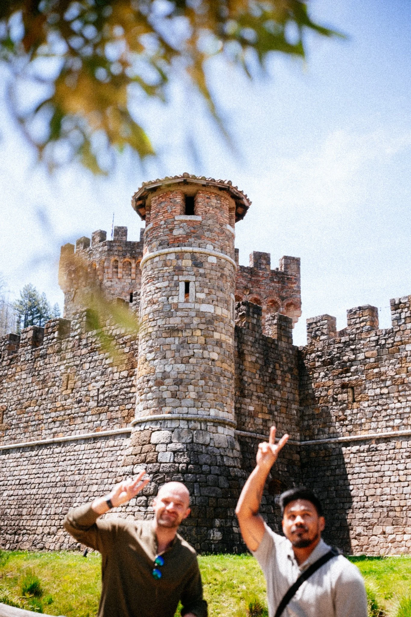 Two friends flashing peace signs below the stone towers of Castello di Amorosa