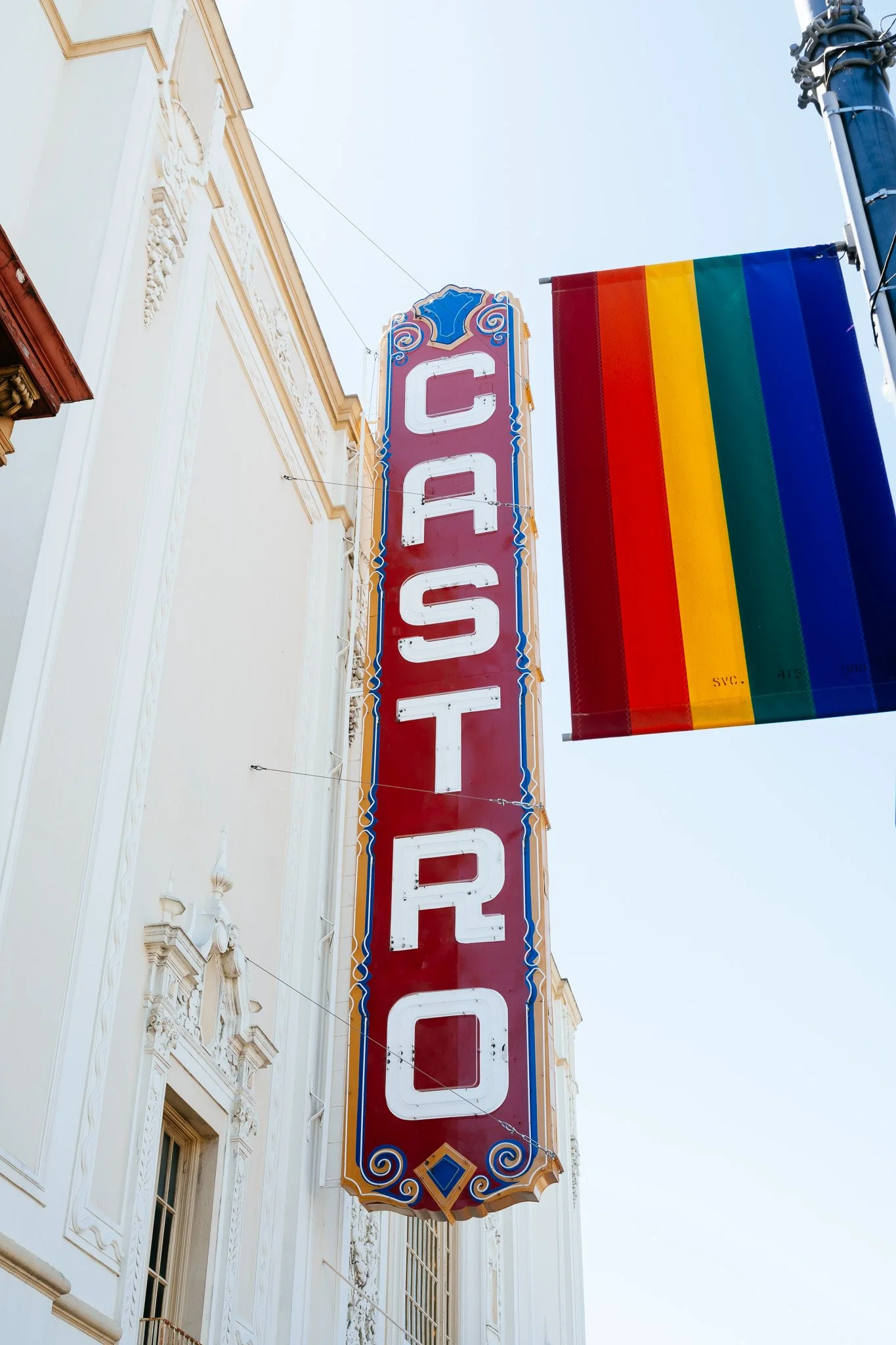Castro Theatre marquee sign beside a rainbow flag banner against a bright sky