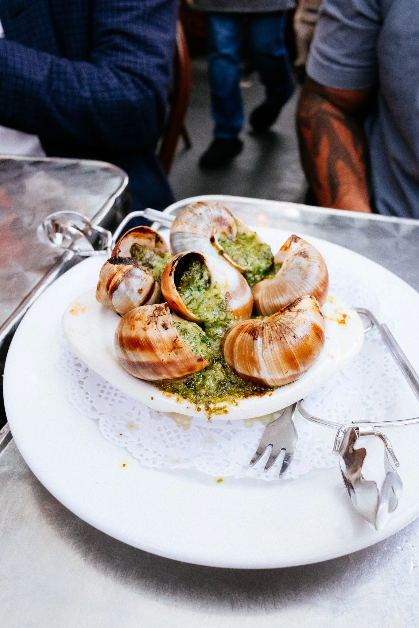 Plate of escargots in green garlic-herb butter with a small fork on a doily